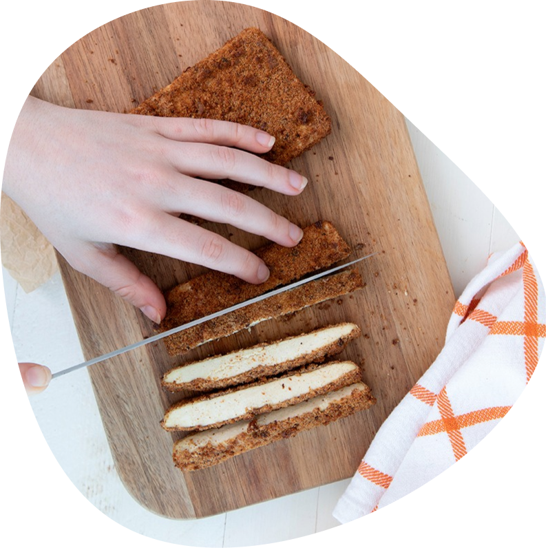 Hand slicing crispy sprouted breadcrumb-crusted tofu katsu cutlets on a wooden board